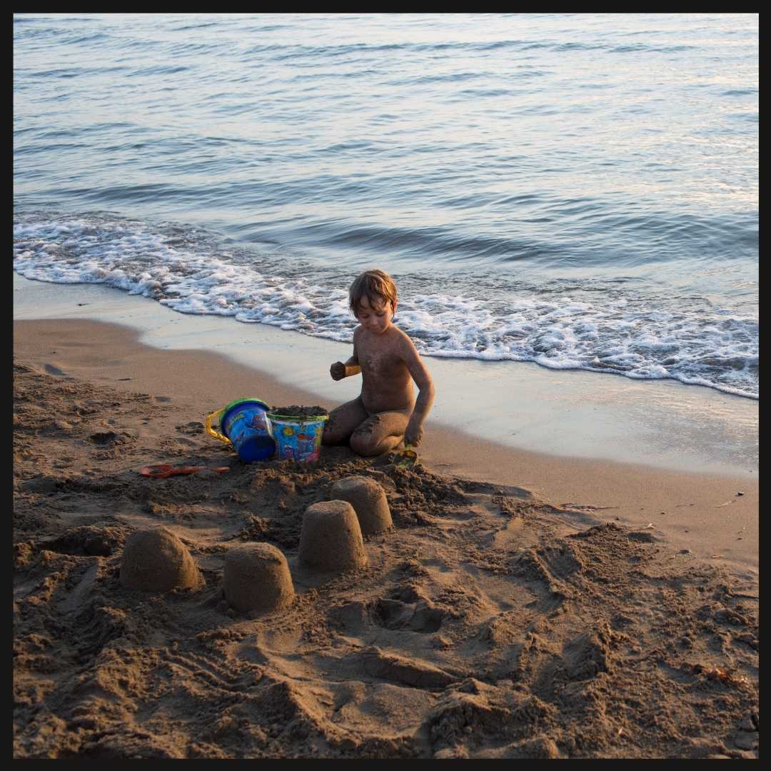 Young girl child making sandcastles at the beach